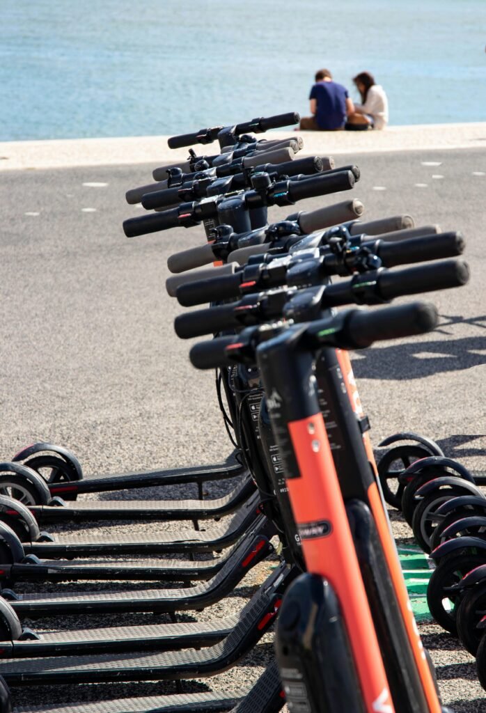 A row of electric scooters parked near Lisbon's waterfront with a couple sitting by the sea.
